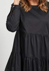 Schwarzes, gestuftes knielanges Kleid aus leichtem Stoff, mit Rundhalsausschnitt und geknöpften Ärmeln sowie einer leicht gerafften Textur.