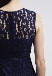 Navy blue lace dress featuring floral patterns, a fitted waist, and a back zipper closure. Includes a smooth fabric lining for comfort.