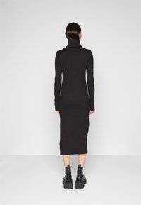 Svart långärmad klänning med hög krage, smal passform och knälång design. Har ribbad textur och kontrasterande axeldetaljer.