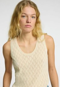 Strikket tanktop i lys beige med bølge mønster tekstur og en rund halsudskæring. Uden ærmer design forbedrer åndbarheden.