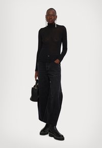 Top negru cu mânecă lungă și guler, asortat cu blugi negri largi, bocanci negri masivi și o geantă mică negrea. Textură de țesătură netedă și transparentă.