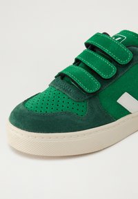 Zelené semišové tenisky s polstrovaným jazykem, třemi suchými zipy, perforovanými síťovinovými detaily a texturovanou gumovou podešví.