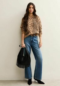 Suéter marrón con manchas, jeans azules, botas de tacón negras hasta el tobillo y un bolso negro con flecos. Textura suave con un corte relajado y patas anchas.