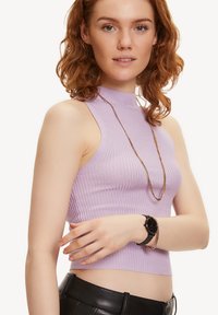 Top sans manches côtelé violet clair avec un col montant. Associé à un pantalon noir slim, une montre noire et un collier en chaîne dorée.