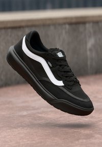 Sorte sneakers med hvite sidestriper, teksturert overdel og flat såle. Har snøring foran, polstret krage og merkevarelogo på tungen.