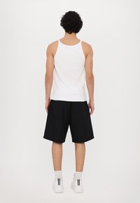 Hvit tanktopp, svarte løse shorts og hvite sneakers sett fra bak. Tanken er ribbet, og shortsene har en avslappet passform. Enkelt design.