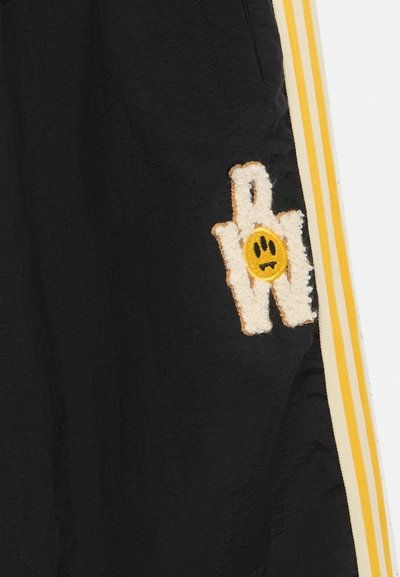 Svart shorts med gule og hvite striper på sidene. Brodert lapper med en hånd og et smilende ansikt.
