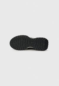 Semelle en caoutchouc noir avec un motif de crampons prononcé, présentant un logo intégré. La surface est texturée et conçue pour l'adhérence et la durabilité.