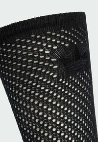 Čierna sieťovaná ponožka s prepracovaným čipkovaným vzorom a čiernym vyšívaným logom Adidas trefoil blízko horného lemu.