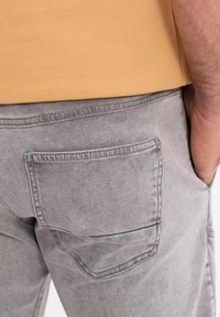 Pantalones de mezclilla gris con un detalle en el bolsillo trasero. La tela tiene una textura ligeramente desgastada y se combina con una blusa de color naranja claro.