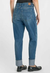 Jeans en denim bleu clair avec une coupe décontractée, ourlet roulé et deux poches arrière. Présente une étiquette en cuir marron au niveau de la taille.