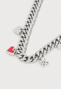 Hõbedast ketiga kaelakee, millel vahelduvad lülid, kaks südamekujulist ripatsit (üks punane, üks hõbedane) ja väike "HUGO" silt.