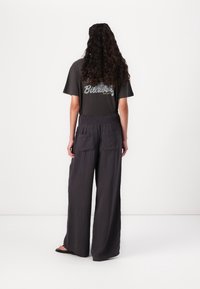 Maglietta grigia scura con logo "Billabong", abbinata a pantaloni neri larghi e strutturati con due tasche posteriori. Calzature semplici in formato sandalo.