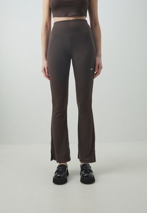 Femme portant des leggings évasés marron foncé taille haute avec un petit logo Nike blanc, des mocassins à plateforme noirs brillants et un top court.