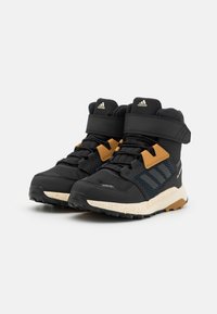 Scarpe sportive alte nere con parte superiore texturizzata, dettagli arancioni e suola bianca maculata. Presentano un sistema di chiusura sicuro con fibbia e lacci.