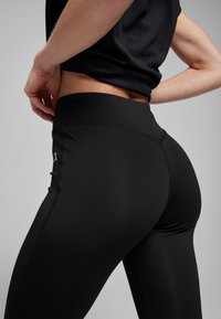 Zwarte sportlegging van rekbaar materiaal, met een hoge tailleband en naden langs de zijkanten voor een aangesloten silhouette.