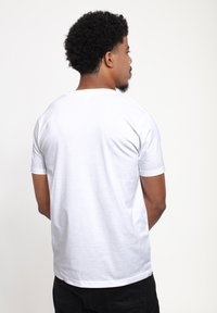 Camiseta blanca de manga corta con cuello redondo y textura suave, vista desde atrás, combinada con pantalones oscuros.