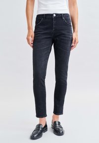 Vaqueros negros ajustados de talle medio, con diseño de cinco bolsillos y cierre de botón. Textura de denim suave con un ligero desgaste.