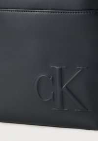 Τσάντα από δέρμα σε ναυτικό μπλε χρώμα με ανάγλυφο λογότυπο "CK", λεία υφή και ακριβείς ραφές. Μινιμαλιστικός σχεδιασμός με κομψό φινίρισμα.