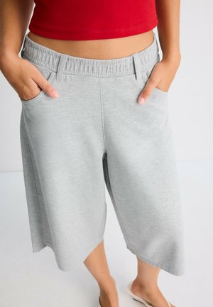 Persona che indossa pantaloncini ampi grigio chiaro con vita elastica e tasche, abbinati a un top corto rosso e sandali beige.