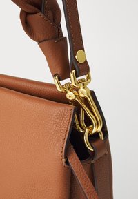 Brown leather handbag with a textured finish. Features a braided strap and gold hardware accents, including a clasp and ring detail.
