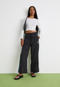 Black wide-leg pants with teal side stripes and a drawstring waist. Paired with a fitted, cropped, ribbed long-sleeve top in light grey.