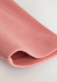 Nahaufnahme eines gerippten pinken Stoffarmels mit sichtbarer Naht und gefaltetem Bündchen auf einem einfachen hellen Hintergrund.