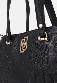 Zwarte leren handtas met een gegraveerd bloemenontwerp, gouden hardware, dubbele handvatten en een centrale sluitsluiting. Getextureerde oppervlakte met intrikate patronen.