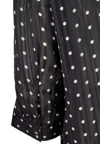 Blusa nera trasparente con pois bianchi. Caratterizzata da maniche lunghe e polsini con bottoni. Tessuto a trama con strisce verticali sullo sfondo.