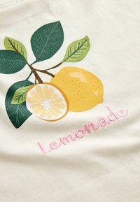 Žlutý citron a plátek citronu se zelenými listy nad růžovým vyšívaným slovem "Lemonade" na bílém plátně.