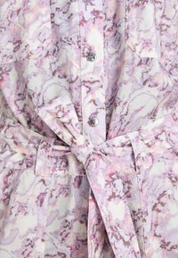 Gros plan d'une robe chemise à motif marbré violet clair et rose, avec des boutons-pression argentés et une ceinture en tissu à nouer à la taille.