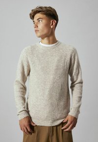 Beżowy sweter z prążkowanego dzianiny z okrągłym dekoltem i długimi rękawami, wykonany z teksturowanej tkaniny, noszony na białej koszuli.