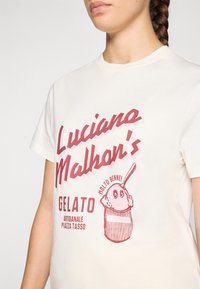 Kremo spalvos medvilninė marškinėliai su raudona grafika, kurioje užrašyta "Luciano Malhon's Gelato" ir iliustruotas ledų ragelis priekyje.