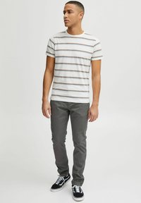 Rutet T-skjorte med korte ermer i lys grå med tynne horisontale striper. Kombinert med grå bukser og svarte joggesko. Enkel, uformell stil.