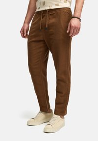 Braune, strukturierte Chinos mit elastischem Bündchen und Kordelzug. Gerade geschnitten mit Seitentaschen. Tragen mit beigen Sneakers.