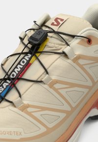 GORE-TEX trkačke tenisice u bež boji s teksturiranim uzorkom, koje imaju brzi sustav vezivanja i obojeni logo branda sa strane.