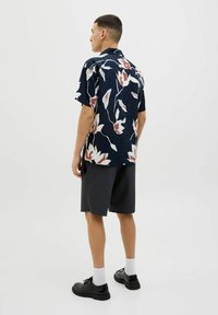 Camisa de manga corta azul marino con un estampado floral en blanco y coral, combinada con pantalones cortos oscuros. El modelo lleva zapatos negros y calcetines blancos.