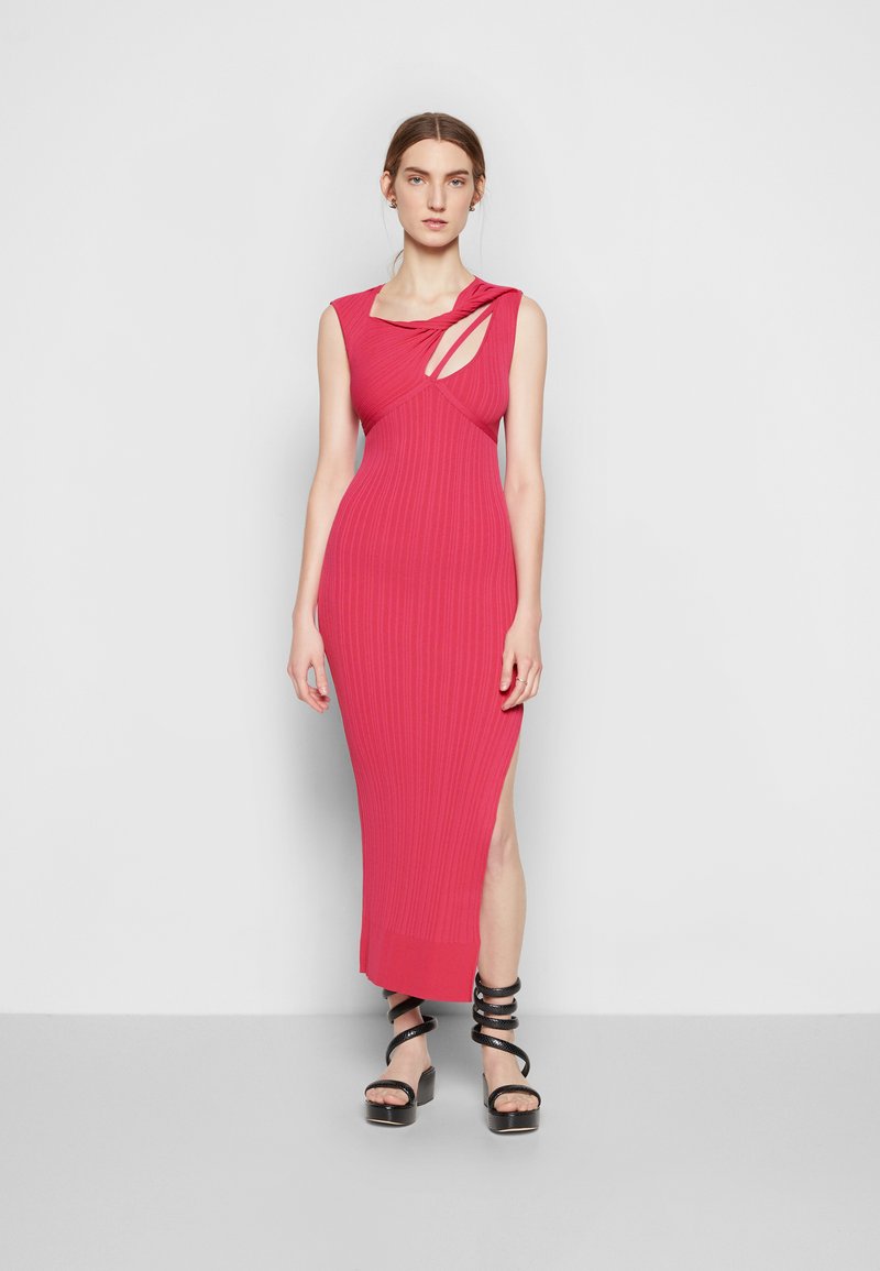 Robe midi ajustée et côtelée en rose vif, avec un col torsadé et une fente sur le côté. Associée à des sandales à plateforme noires à lanières.