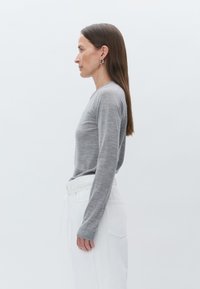 Pull en maille gris à manches longues avec un col rond, associé à un pantalon blanc taille haute. Le matériau semble doux et lisse.