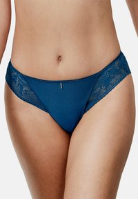 String en dentelle et maille teal avec des bordures en dentelle florale et un petit détail métallique au centre avant. Texture douce et design taille basse.