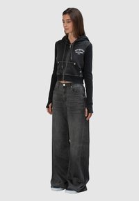 Przycięta czarna bluza z kapturem z prążkowanymi mankietami i przednimi kieszeniami. Połączona z szerokimi, ciemnoszarymi dżinsami. Oba elementy charakteryzują się minimalistycznymi detalami.