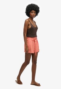 Brown knit tank top paired with light pink belted shorts, featuring side pockets and a relaxed fit. Model wears brown slide sandals.