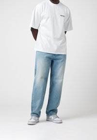 Valkoinen puuvillainen t-paita, jossa rintalogo, yhdistetty vaaleansinisiin farkkuihin. Jalkineina harmaat ja valkoiset lenkkarit. Yleisesti rento istuvuus.