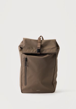 Zaino marrone con chiusura roll-top, tasca frontale con zip e chiusura con fibbia, realizzato in materiale liscio, posizionato su uno sfondo chiaro e uniforme.