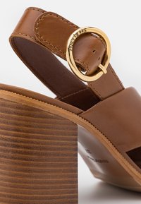 Sandale à talon en cuir marron avec une large bride, une boucle ovale dorée gravée "See By Chloé", et un talon bloc en bois empilé.