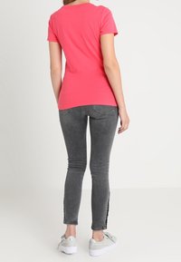 Camiseta de algodón rosa ajustada con mangas cortas, combinada con jeans ajustados grises con aberturas laterales y zapatillas plateadas.