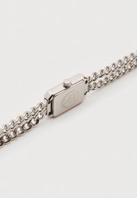 Srebrny zegarek o prostokątnej kopercie, metalowy pasek z ogniwami w formie łańcucha oraz koronką do ustawiania czasu. Prosty i nowoczesny.