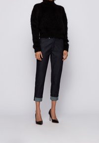 Suéter negro de peluche, jeans de mezclilla oscuros con puños estampados, y tacones negros de punta. Atuendo casual pero refinado.