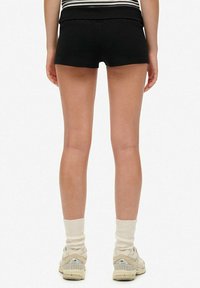 Shorts deportivos negros con un diseño ajustado, textura suave y una cintura alta, combinados con zapatillas beige y calcetines blancos.