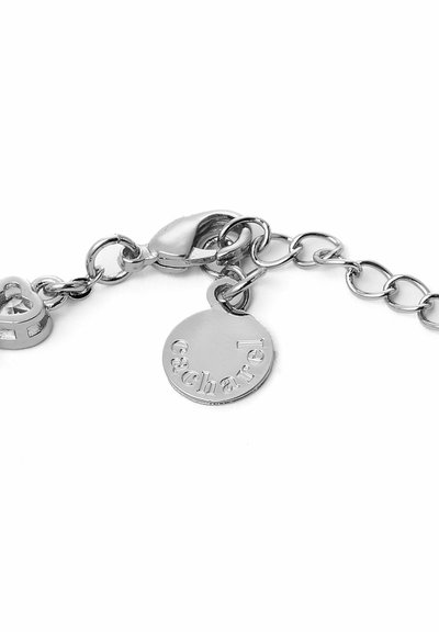 Pulsera metálica plateada con un cierre, una etiqueta circular grabada con "Cacharel" y un charm en forma de corazón. Textura suave y diseño de eslabones.
